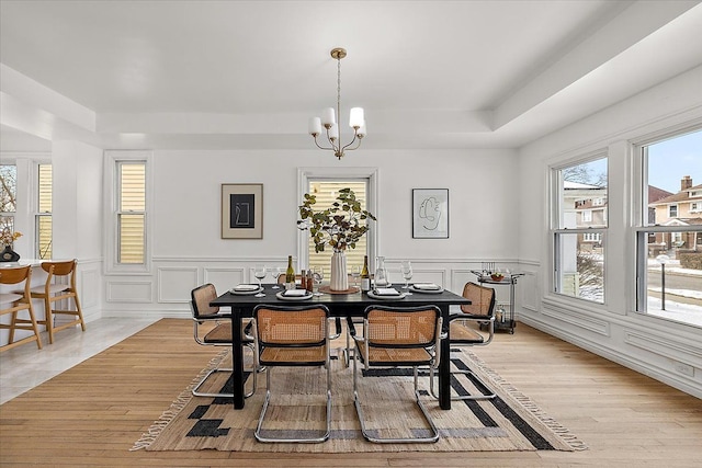 dining space with a raised ceiling, light hardwood / wood-style flooring, and a notable chandelier