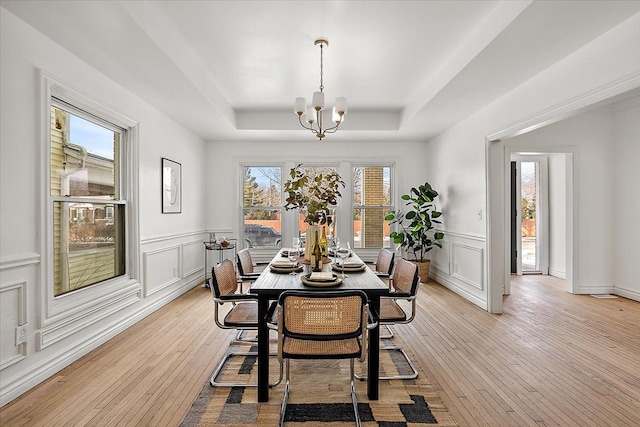 dining space with an inviting chandelier, a tray ceiling, and light hardwood / wood-style flooring