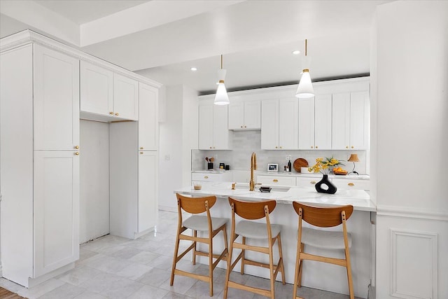 kitchen with a breakfast bar, pendant lighting, white cabinetry, an island with sink, and backsplash