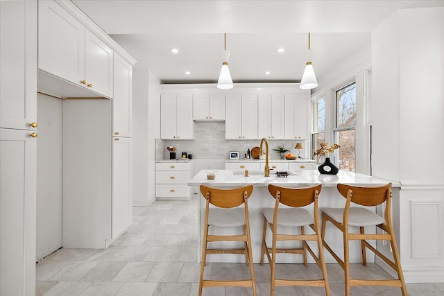 kitchen with pendant lighting, a kitchen island with sink, backsplash, a kitchen breakfast bar, and white cabinets