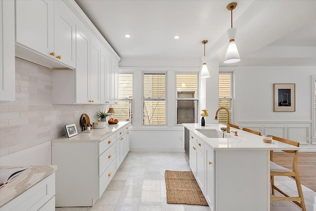 kitchen with a center island with sink, white cabinetry, sink, and pendant lighting