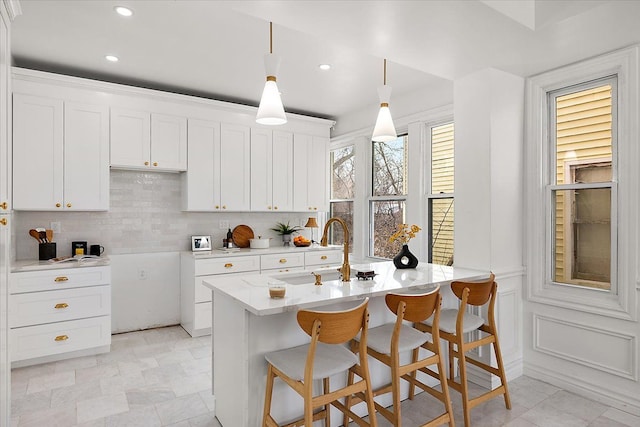 kitchen featuring sink, white cabinetry, hanging light fixtures, tasteful backsplash, and a center island with sink