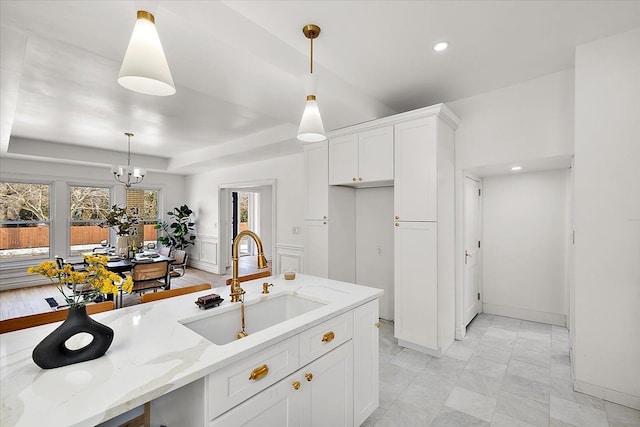 kitchen with light stone counters, sink, hanging light fixtures, and white cabinets