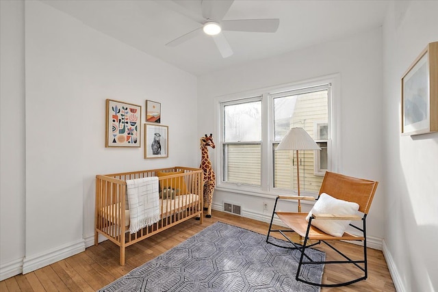 bedroom with hardwood / wood-style flooring, a nursery area, and ceiling fan