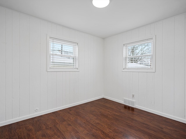 spare room featuring dark hardwood / wood-style flooring, a wealth of natural light, and wood walls