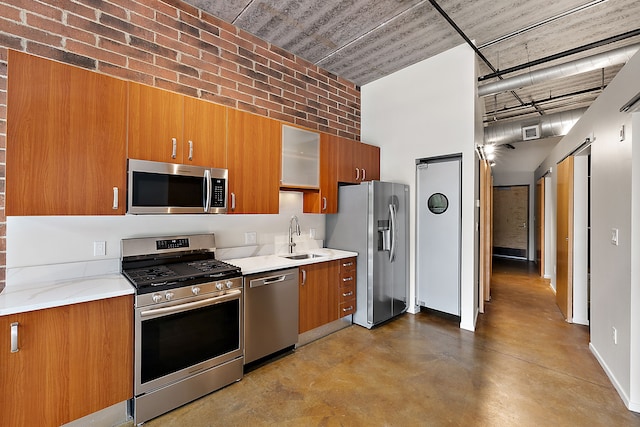 kitchen with a high ceiling, brick wall, appliances with stainless steel finishes, light stone countertops, and sink