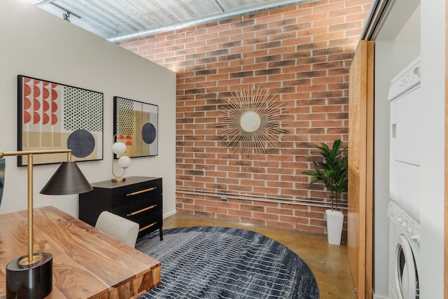 office space featuring brick wall and stacked washer and clothes dryer