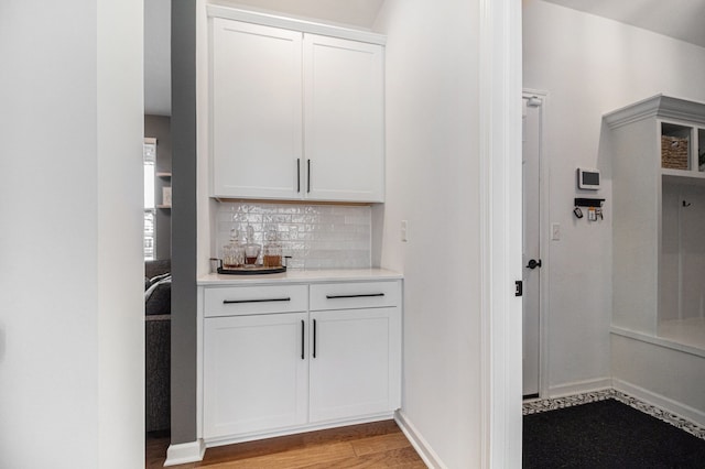 bar with tasteful backsplash, white cabinets, and light wood-type flooring