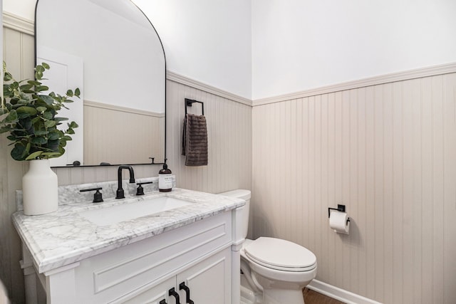 bathroom with vanity, wood walls, and toilet