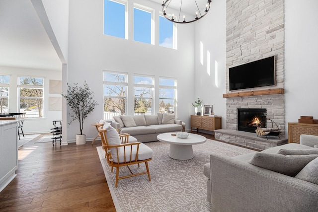 living room with an inviting chandelier, wood-type flooring, a stone fireplace, and a high ceiling