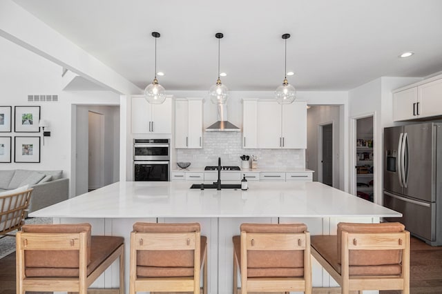 kitchen featuring pendant lighting, white cabinetry, a kitchen breakfast bar, a kitchen island with sink, and stainless steel appliances