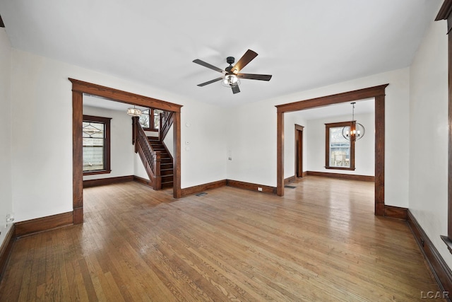 empty room with wood-type flooring and ceiling fan with notable chandelier