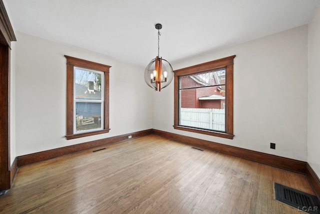 unfurnished dining area with wood-type flooring and an inviting chandelier