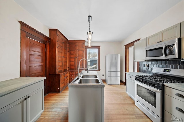 kitchen with decorative light fixtures, tasteful backsplash, sink, light wood-type flooring, and appliances with stainless steel finishes