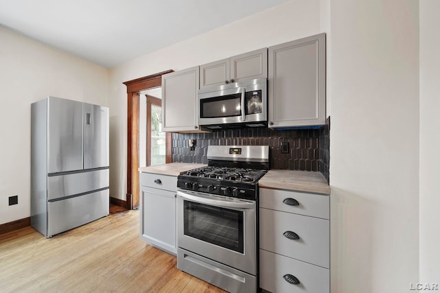 kitchen with light wood-type flooring, appliances with stainless steel finishes, gray cabinetry, and backsplash