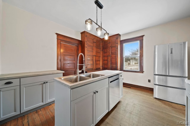 kitchen featuring gray cabinets, an island with sink, stainless steel appliances, decorative light fixtures, and sink