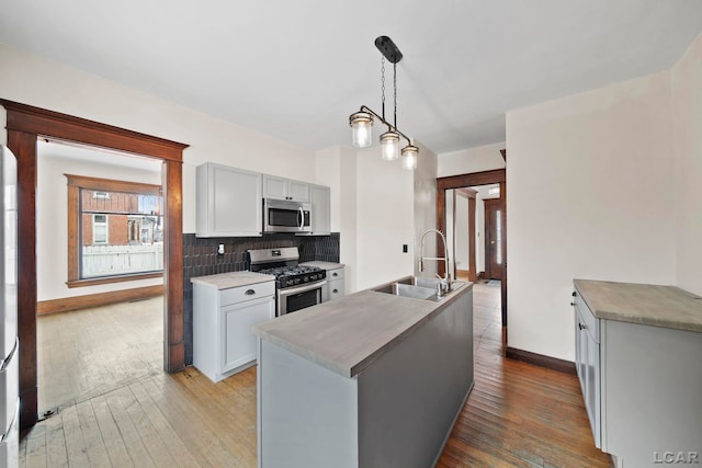 kitchen with decorative light fixtures, stainless steel appliances, tasteful backsplash, an island with sink, and sink