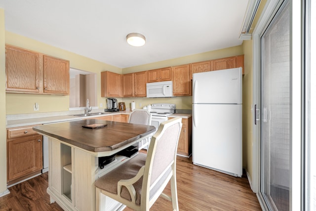 kitchen with sink, white appliances, hardwood / wood-style floors, a kitchen island, and a kitchen bar