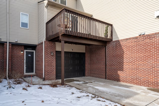 snow covered property entrance with a balcony and a garage