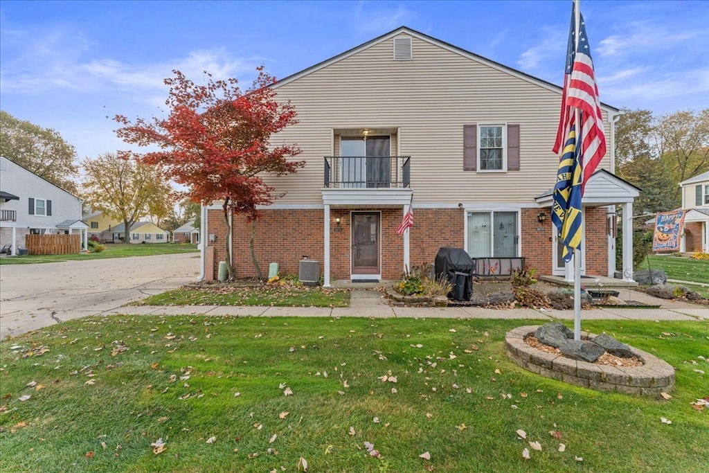 view of front of property featuring a balcony, a front yard, and central air condition unit