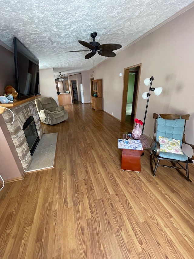 living room featuring ceiling fan, a fireplace, hardwood / wood-style floors, and a textured ceiling