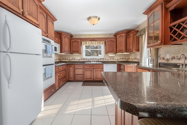 310 Sycamore St, Litchfield, MI 49252 - kitchen featuring a sink, brown cabinets, glass insert cabinets, light tile patterned floors, and white appliances