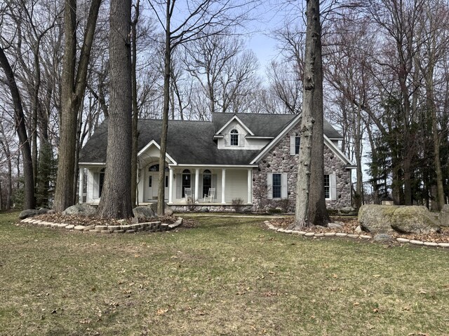 310 Sycamore St, Litchfield, MI 49252 - view of front of home featuring a shingled roof, a front yard, covered porch, and stone siding