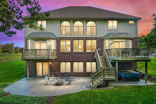 back house at dusk featuring a lawn, a deck, an outdoor fire pit, a patio area, and a hot tub