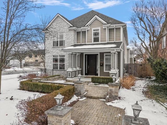 traditional-style home with a shingled roof, covered porch, and fence