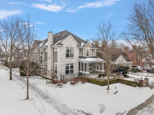 snow covered house with stone siding and a chimney