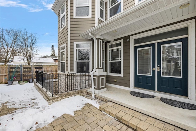 snow covered property entrance with covered porch and fence