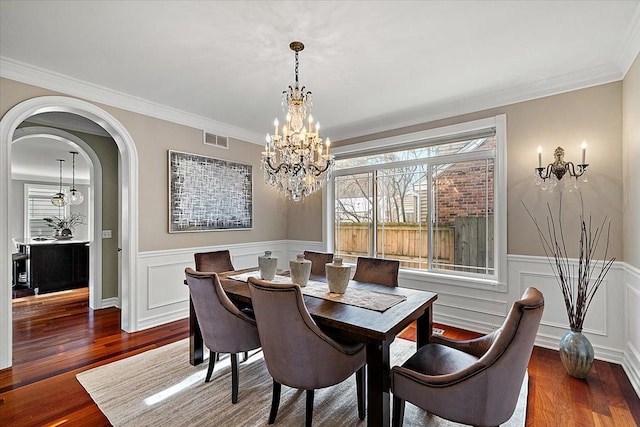 dining room with arched walkways, a notable chandelier, wood finished floors, visible vents, and wainscoting