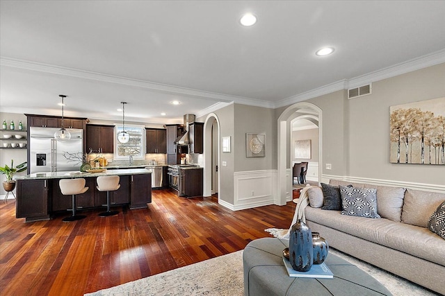 living area featuring arched walkways, recessed lighting, visible vents, ornamental molding, and dark wood-style floors