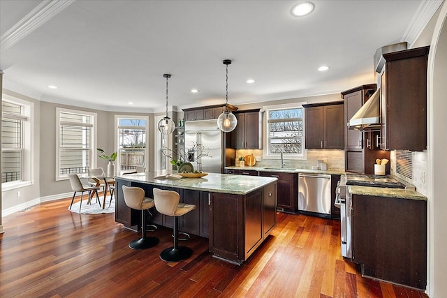 kitchen with dark brown cabinetry, high end appliances, a kitchen island, crown molding, and a sink