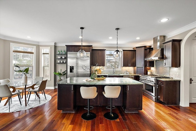 kitchen with premium appliances, a center island, a sink, dark brown cabinets, and wall chimney exhaust hood