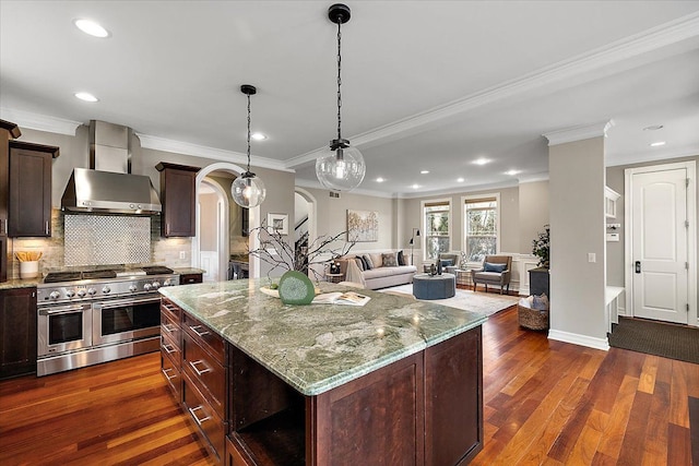 kitchen featuring range with two ovens, arched walkways, dark wood-style floors, backsplash, and wall chimney range hood