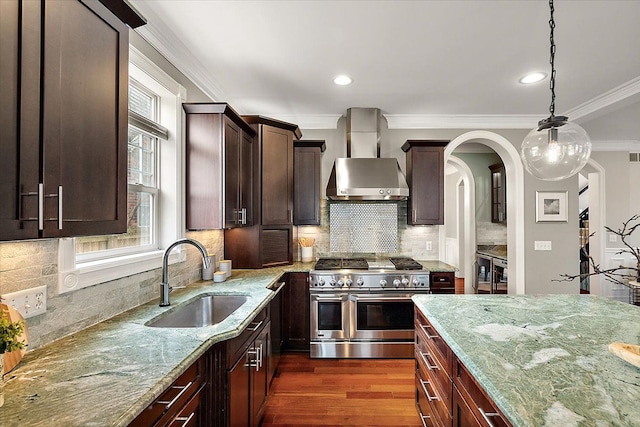 kitchen featuring range with two ovens, light stone counters, dark wood finished floors, a sink, and wall chimney exhaust hood