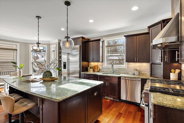 kitchen featuring dark wood finished floors, premium appliances, wall chimney exhaust hood, ornamental molding, and a sink