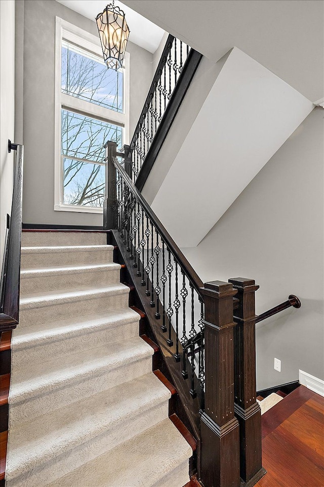 stairway with a notable chandelier, a towering ceiling, baseboards, and wood finished floors