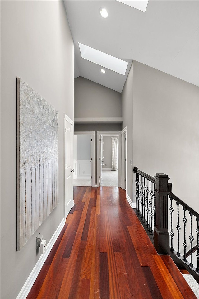 hall with high vaulted ceiling, recessed lighting, a skylight, wood finished floors, and baseboards