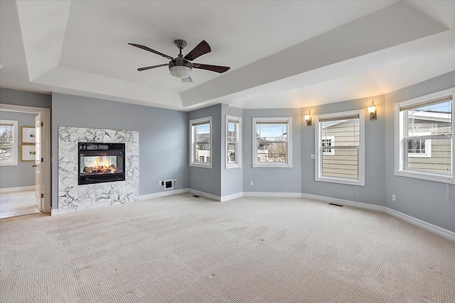 unfurnished living room featuring a high end fireplace, a raised ceiling, light colored carpet, and plenty of natural light