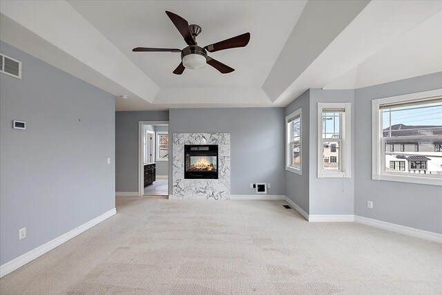 unfurnished living room with a raised ceiling, visible vents, baseboards, and a premium fireplace