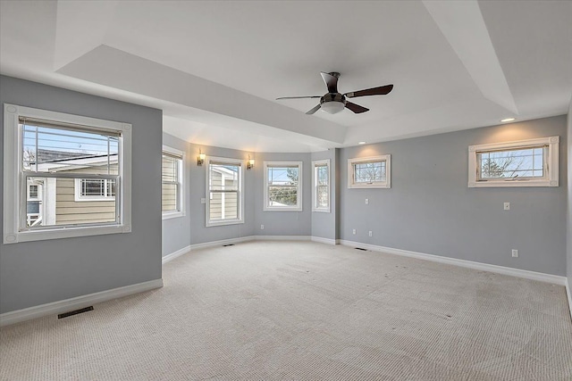 spare room featuring light carpet, a tray ceiling, and baseboards