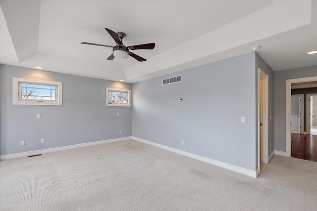 empty room with a raised ceiling, visible vents, ceiling fan, and baseboards