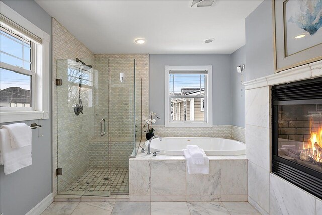 full bathroom with a garden tub, a shower stall, a wealth of natural light, and a glass covered fireplace