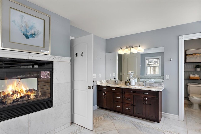 bathroom with marble finish floor, double vanity, toilet, a high end fireplace, and a sink