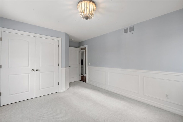 unfurnished bedroom with a closet, visible vents, light carpet, and wainscoting