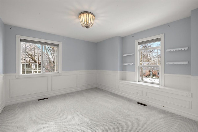 unfurnished room featuring wainscoting, carpet flooring, and a healthy amount of sunlight