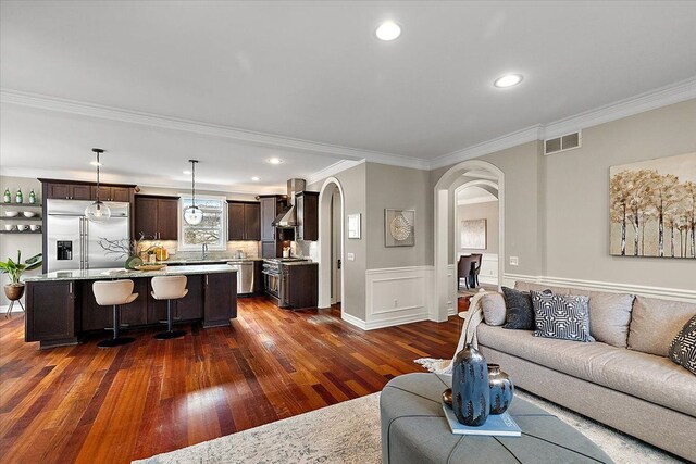 living area featuring visible vents, arched walkways, dark wood-style floors, crown molding, and recessed lighting