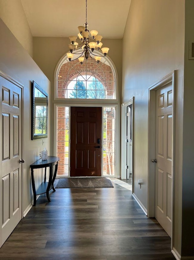 entryway with visible vents, baseboards, dark wood-type flooring, an inviting chandelier, and a high ceiling